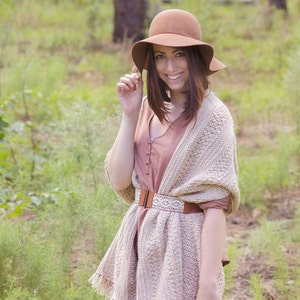 A woman wearing a cream crochet shawl wrap and hat, in a field of greenery.