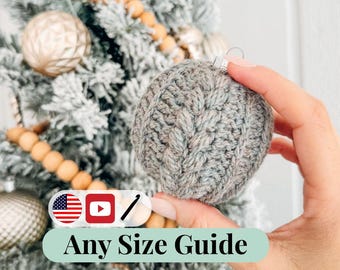Könnte beinhalten: Ein grauer, gestrickter Weihnachtsschmuck mit einem strukturierten Muster wird vor einem geschmückten Weihnachtsbaum gehalten. Der Schmuck ist rund und hat eine silberne Metallkappe. Der Text "Any Size Guide" wird auf einem hellgrünen Banner angezeigt.