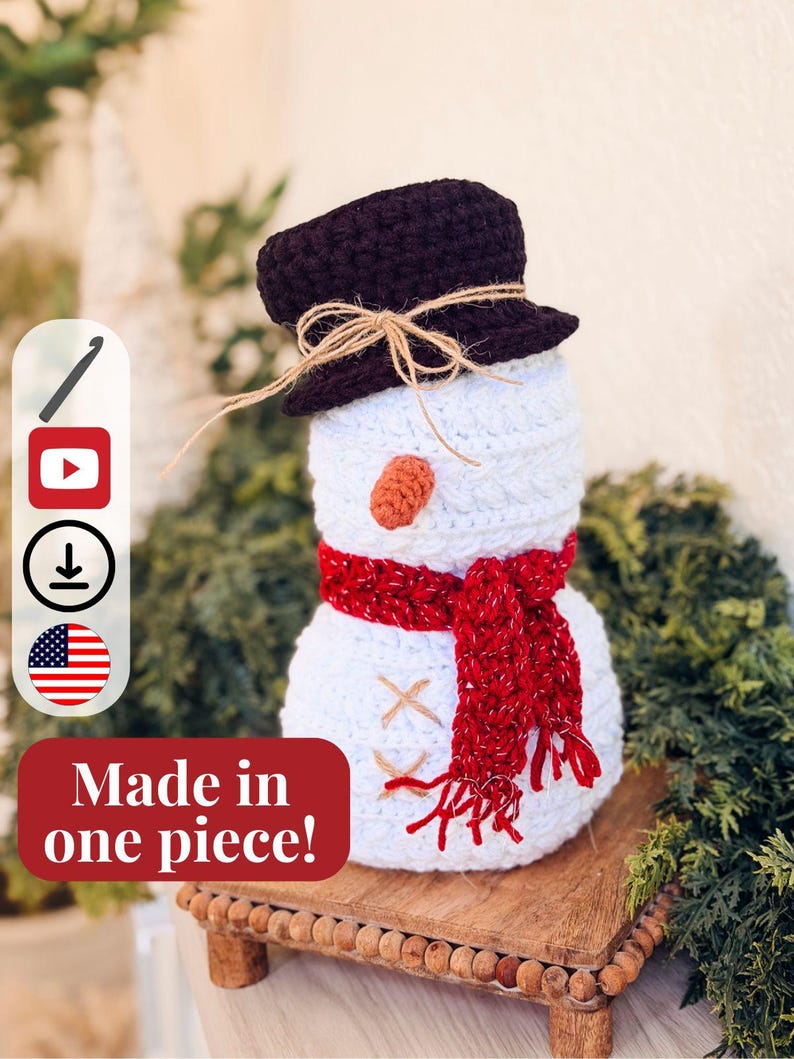 White crochet snowman with brown top hat, red scarf and carrot nose on a wooden riser, with icons and a made in one piece banner