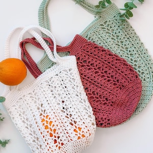 Puede incluir: Tres bolsas de mano de ganchillo en blanco, burdeos y verde salvia. La bolsa blanca contiene naranjas. Las bolsas tienen asas largas y patrones de tejido abierto. Ramas de eucalipto en el fondo. Estas bolsas reutilizables son perfectas para ir de compras.