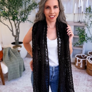 May include: A long, black crochet scarf featuring an open, airy, and intricate web-like pattern. The scarf is draped vertically around the neck, showcasing the detailed, lightweight yarn construction and the consistent, repeating geometric stitch design.