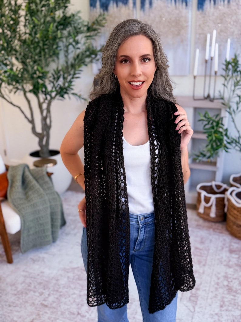 May include: A long, black crochet scarf featuring an open, airy, and intricate web-like pattern. The scarf is draped vertically around the neck, showcasing the detailed, lightweight yarn construction and the consistent, repeating geometric stitch design.
