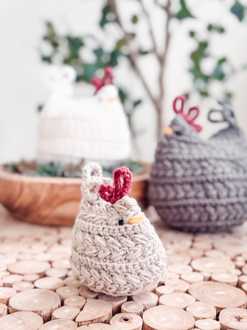Small oatmeal crochet chicken with braided texture on wood slices, with white and gray hens blurred behind