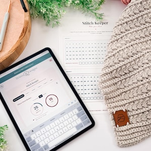 May include: A tablet displaying the Briana K Designs Stitch Keeper app, a printed Stitch Keeper tracking sheet, and a beige crocheted fabric piece with a brown leather tag featuring a logo, alongside yarn balls and a crochet hook.