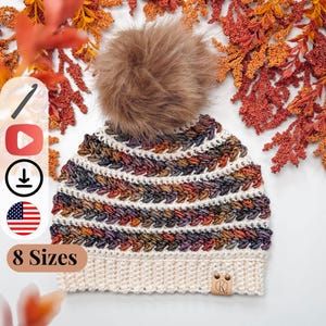 A crocheted hat with multicolored stripes, a white brim, and a large brown pom-pom is displayed on a white surface with orange and yellow foliage, perfect as a cozy handmade gift. Text indicates "8 Sizes.”