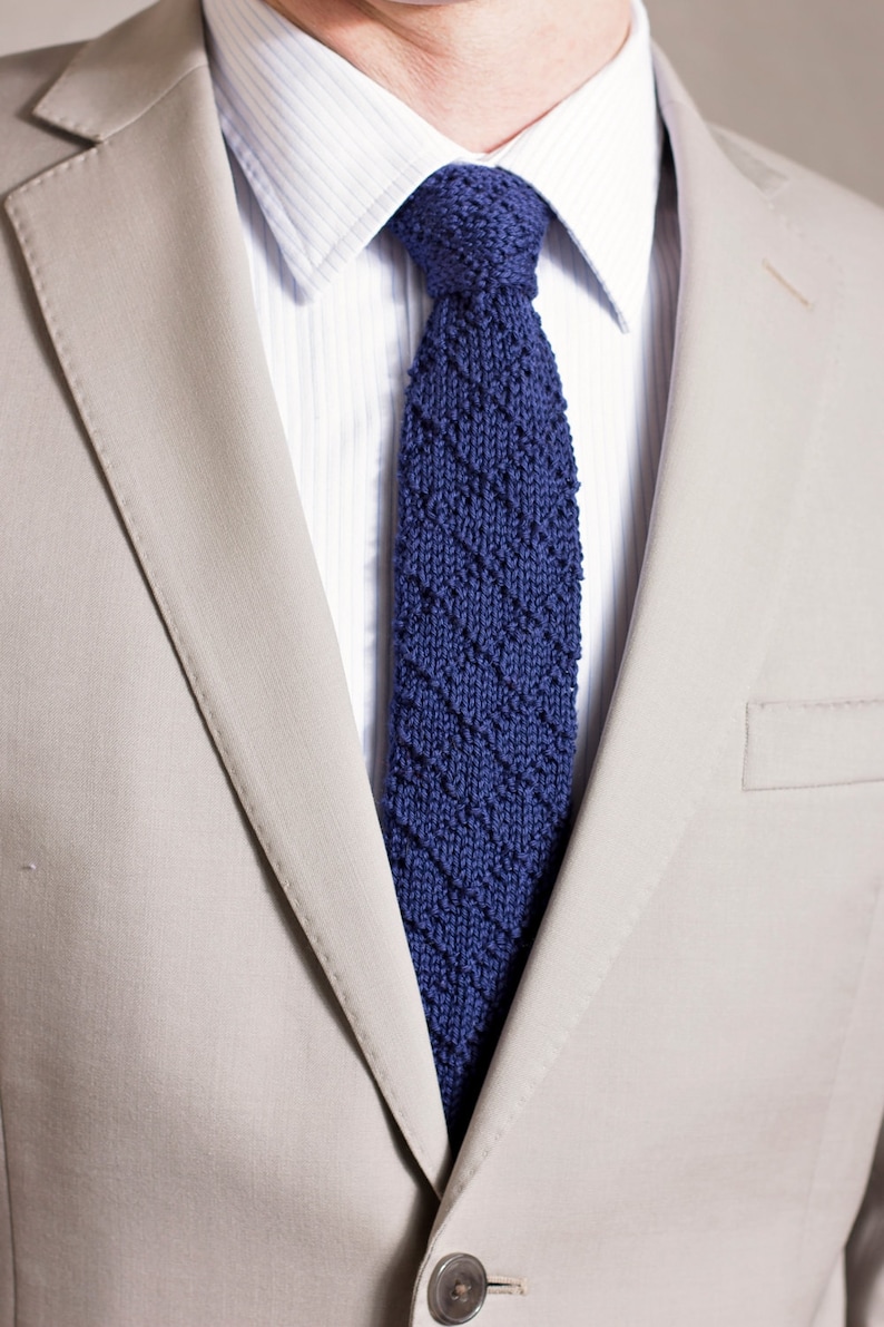 May include: A beige suit jacket with a blue knitted tie. The tie has a diagonal pattern.