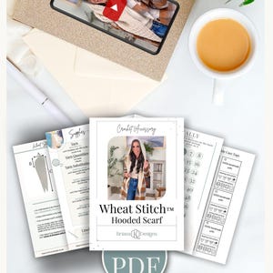 May include: A selection of crochet accessory patterns, including a "Wheat Stitch Hooded Scarf" design, with care tags and yarn information. A video on a phone shows the scarf. A cup of tea and a pen are also visible.