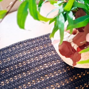 A cream-colored vase with red and green foliage sits on a wooden table with a dark woven table runner, creating the perfect setting for displaying unique jewellery or presenting a thoughtful handmade gift.