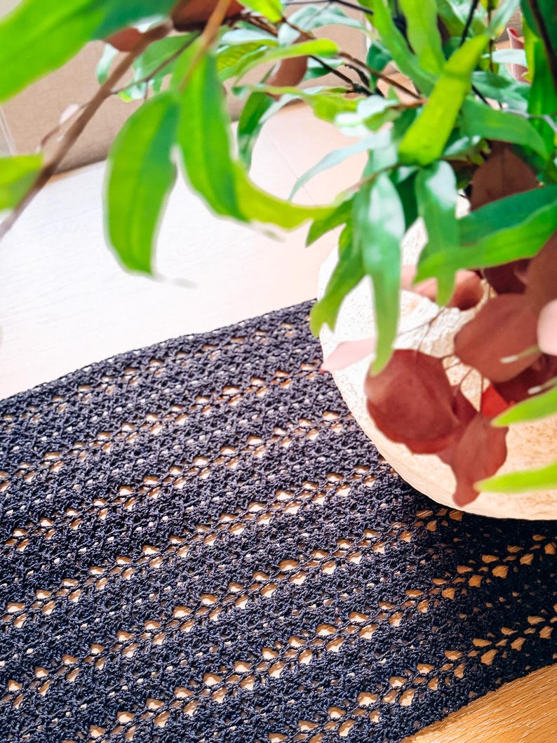A cream-colored vase with red and green foliage sits on a wooden table with a dark woven table runner, creating the perfect setting for displaying unique jewellery or presenting a thoughtful handmade gift.