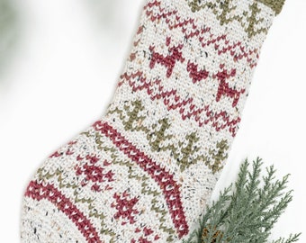 May include: A white, green, and red knitted Christmas stocking with a green crocheted cuff and a brown leather loop. The stocking has a traditional fair isle pattern with reindeer and snowflakes.