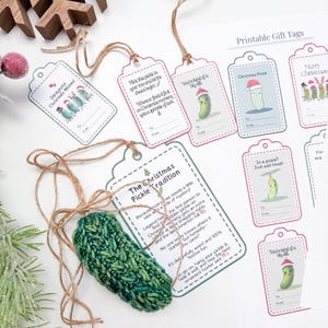 May include: A crocheted green pickle ornament with twine, accompanied by a sheet of printable gift tags featuring pickle illustrations and text including "The Christmas Pickle Tradition," "Dill-lightful Christmas Wishes," and "In a pickle?"