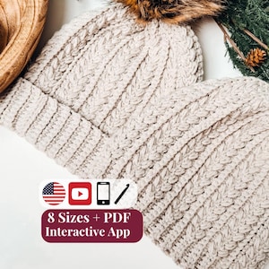 May include: Two cream-colored crocheted beanies with ribbed textures and brown faux fur pom-poms. A graphic overlay displays the text 8 Sizes + PDF Interactive App, accompanied by icons of a US flag, a play button, a smartphone, and a crochet hook.