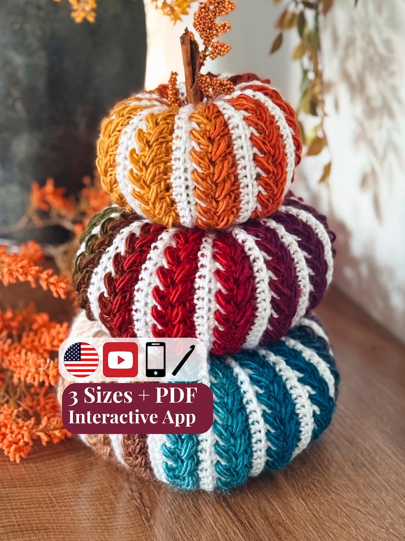 Three stacked crochet pumpkins in gold, red, and teal with white braided stripes beside orange fall stems