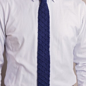 May include: A white dress shirt with a blue knitted tie. The shirt has a striped pattern and the tie has a diagonal pattern.
