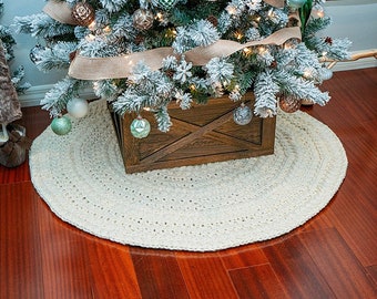 May include: A white crocheted Christmas tree skirt with a rustic wooden tree stand underneath a flocked Christmas tree.