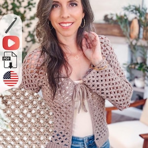May include: A beige crochet cardigan featuring a repeating openwork diamond pattern, long sleeves, and a front tie closure. The garment has a ribbed hem and cuffs, with a detailed circular inset showing the intricate texture of the yarn stitches.