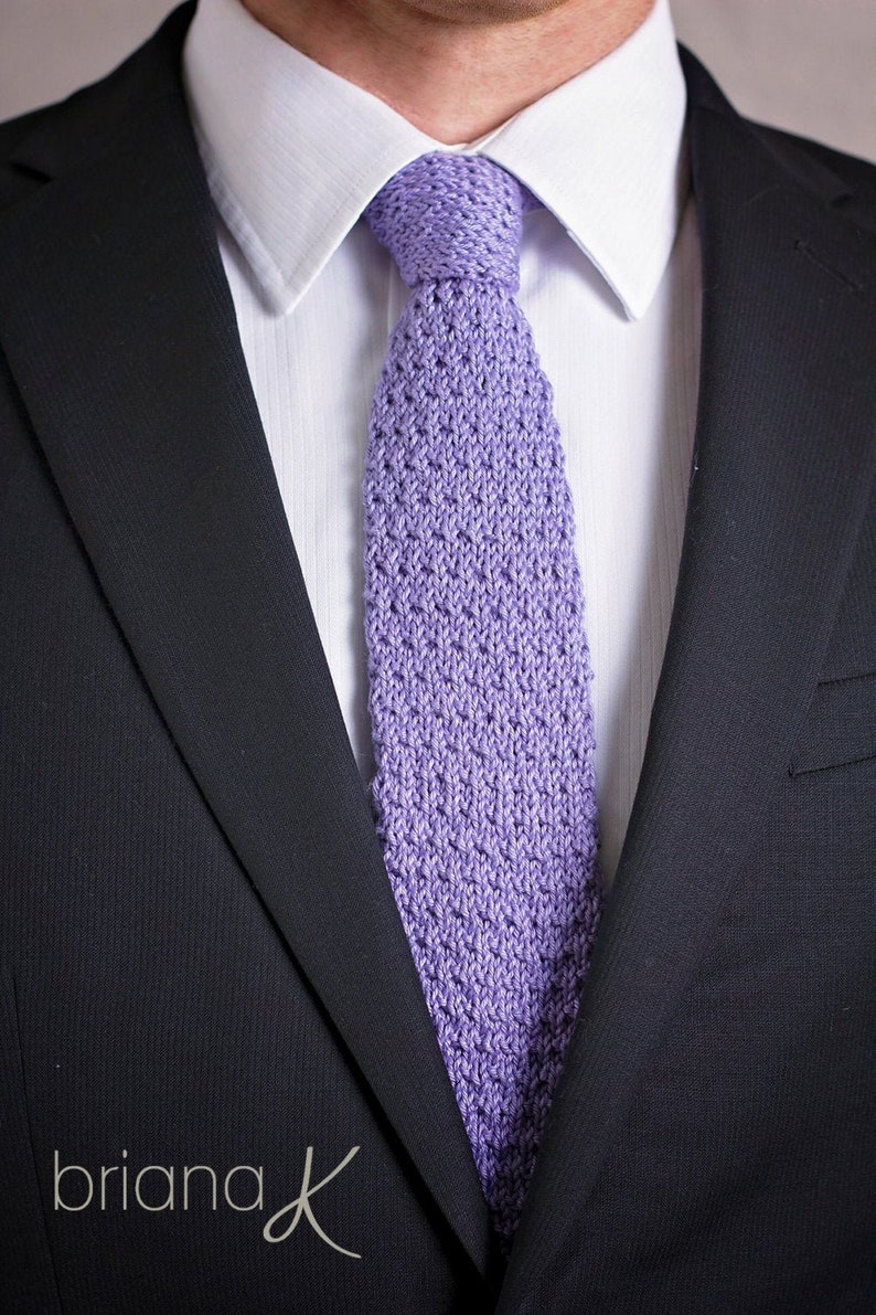 May include: A purple knitted tie worn with a white dress shirt and a dark blue suit jacket.