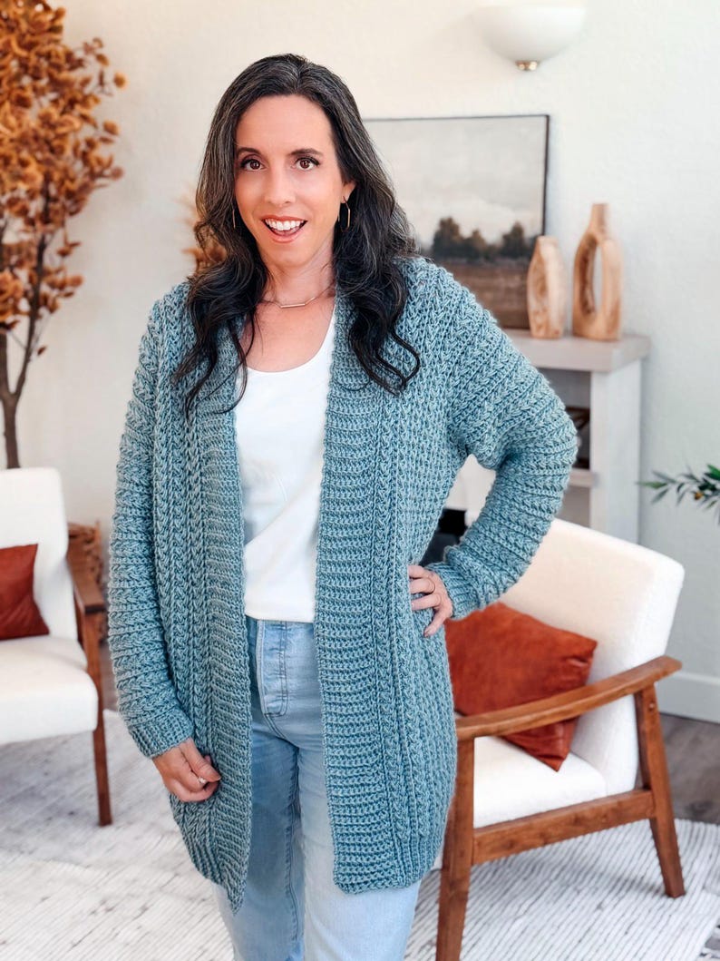May include: A light blue, open-front cardigan with a textured knit design. The long-sleeved sweater is worn over a white top and light blue jeans. The cardigan is knee-length and appears to be handmade.