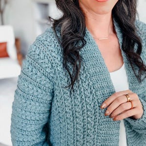 May include: A light blue crochet cardigan with a textured stitch pattern. The open-front sweater has long sleeves and a relaxed fit. The cardigan is a soft, comfortable garment.