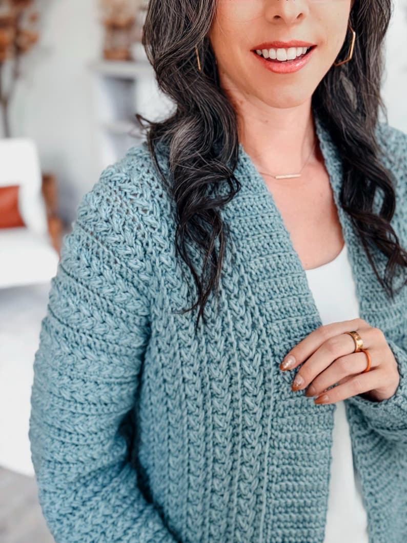 May include: A light blue crochet cardigan with a textured stitch pattern. The open-front sweater has long sleeves and a relaxed fit. The cardigan is a soft, comfortable garment.