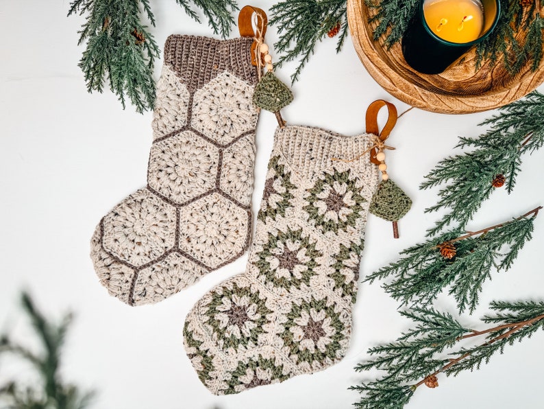 May include: Two handmade crochet stockings featuring intricate yarn patterns. One stocking displays a beige hexagonal motif with brown borders, while the other features a floral-inspired square design in cream, sage green, and brown. Both have leather loops.