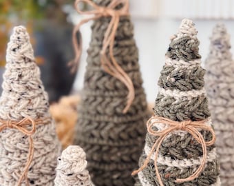 May include: A collection of cone-shaped decorative trees crafted from textured yarn in shades of olive green, cream, and speckled beige. Each tree features a distinct crochet stitch pattern and is accented with a thin, tied tan twine bow.