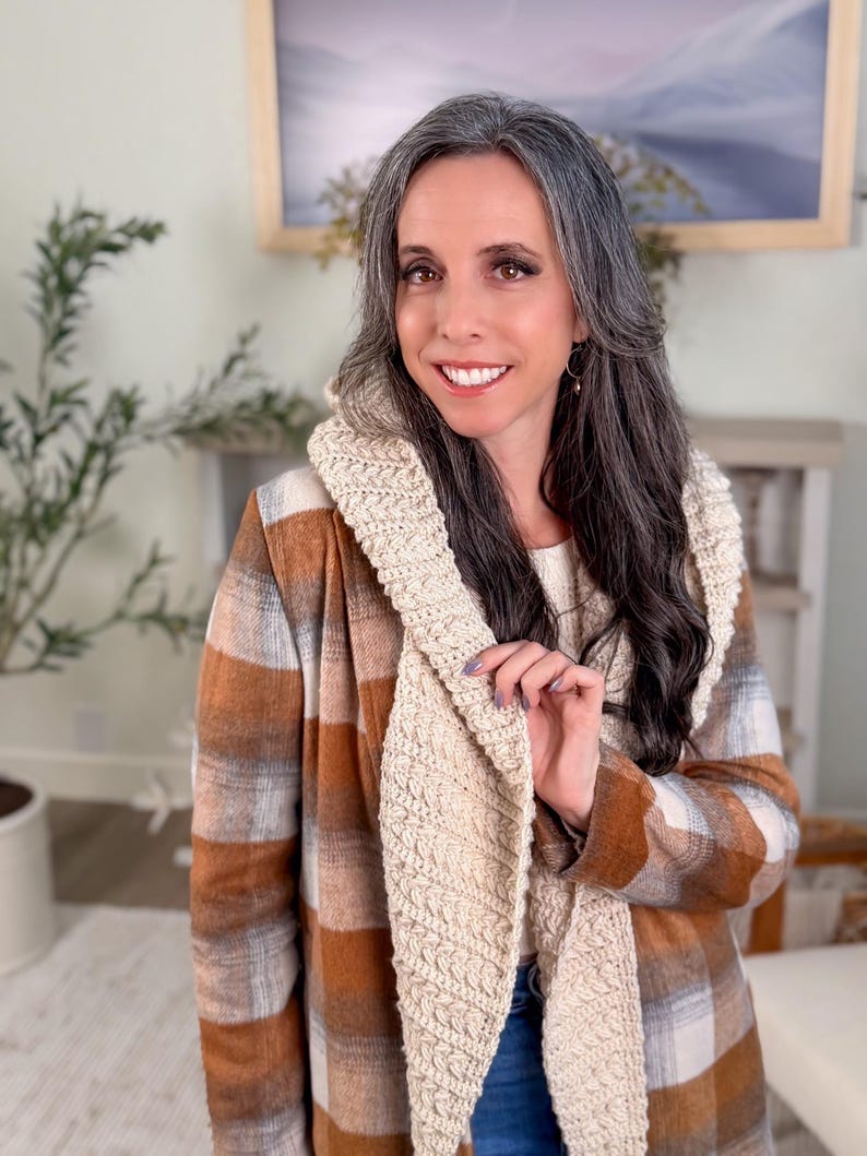May include: A woman wearing a beige and brown checked jacket with a cream-coloured, textured scarf. The jacket has a classic checked pattern. The scarf is a lighter shade and appears to be knitted or crocheted. The woman is smiling.
