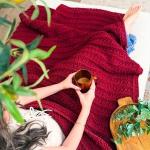 Puede incluir: Una manta de punto grueso en color rojo intenso con una textura acanalada prominente. La manta está colocada sobre una superficie, mostrando su construcción de hilo grueso y un patrón de puntadas verticales constante en toda la pieza.