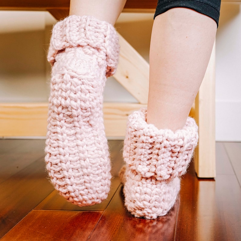 May include: A pair of pink crocheted slipper socks with a folded cuff. The socks are made with a chunky yarn and have a soft, cosy look.
