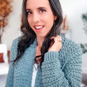 May include: A light blue crochet cardigan with a textured stitch pattern. The open-front sweater has long sleeves and a relaxed fit. The cardigan is worn over a white top.