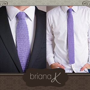 May include: A purple knitted tie with a textured pattern. The tie is worn with a white dress shirt and a dark suit jacket.