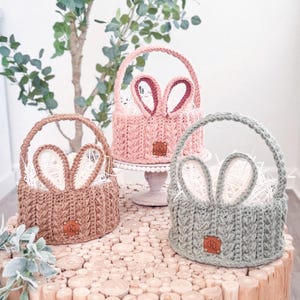 May include: Three crocheted Easter baskets with bunny ears. The baskets are pink, brown, and green. Each basket has a brown leather tag with the initials "CR" on it.