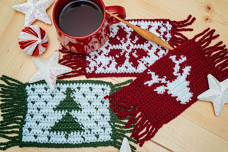 May include: Three crocheted coasters with fringe, featuring a Christmas tree, reindeer, and snowflake designs. The coasters are in red, green, and white yarn.