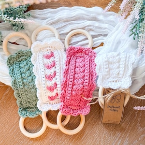 May include: Four handmade crochet dish towel holders in green, white, and pink, each with a wooden ring. The white holder has a tag that reads "Dish towel Holder". The holders are displayed on a white cloth with floral accents.
