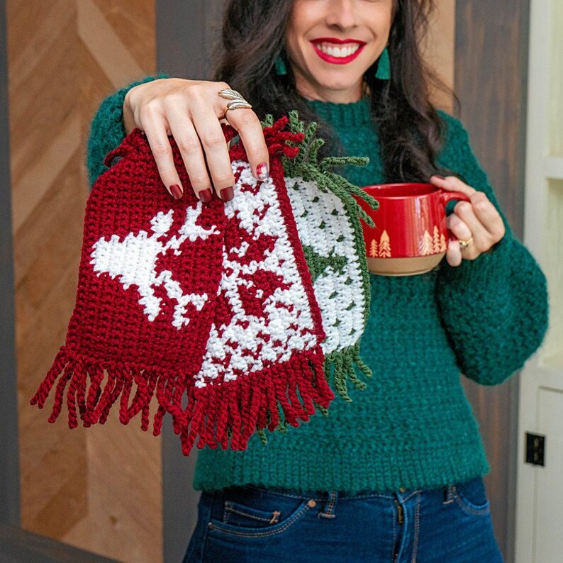 May include: Three crocheted mug cozies with fringe. One is red and white with a snowflake design, one is green and white with a star design, and one is green with a Christmas tree design.