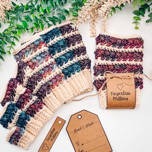 May include: A pair of handmade fingerless mittens in cream, teal, purple, and burgundy. The mittens are crocheted with a textured stitch. A matching pair of mittens and a tag that says "Fingerless Mittens" are displayed with a "Hand Made" tag.