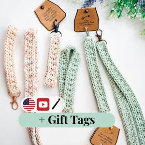 Puede incluir: Varios llaveros de ganchillo hechos a mano en crema, pastel y verde. Cada llavero tiene un cierre de mosquetón y va acompañado de una etiqueta de regalo. Las etiquetas incluyen frases como "Un recordatorio de que eres amado" y "Lleva una puntada de alegría".