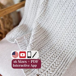 May include: A light gray crocheted blanket with a textured vertical stitch pattern. A brown leather tag with a logo is attached to the corner. An overlay includes icons for the US flag, YouTube, phone, and crochet hook, with text: 16 Sizes + PDF Interactive App.