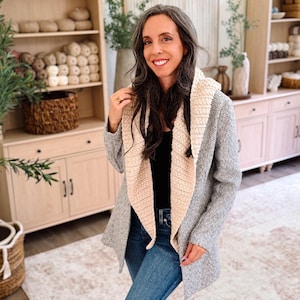 May include: A gray herringbone patterned cardigan featuring a wide, cream-colored textured shawl collar, worn over a black top and blue denim jeans. The garment has long sleeves and an open front design with a soft, knit fabric construction.