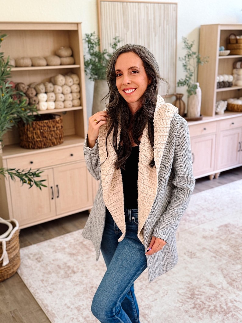 May include: A gray herringbone patterned cardigan featuring a wide, cream-colored textured shawl collar, worn over a black top and blue denim jeans. The garment has long sleeves and an open front design with a soft, knit fabric construction.