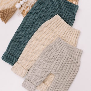 May include: Three pairs of ribbed knit pants in teal, cream, and light gray. Each pair features a high-waisted design with a thick elasticized waistband and cuffed ankles, crafted with a vertical textured stitch pattern throughout the garment.