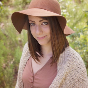 A woman wearing a cream crochet shawl wrap and hat, in a field of greenery.