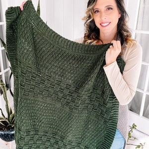 Puede incluir: Una manta rectangular de color verde bosque oscuro con un patr&oacute;n de ganchillo texturizado que presenta secciones alternas de puntos s&oacute;lidos y un dise&ntilde;o de tejido de cesta, terminada con un borde acanalado en los extremos.