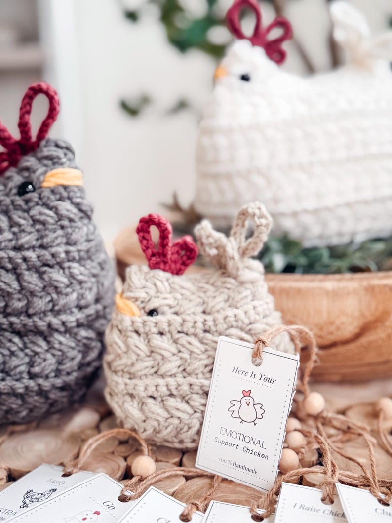 Small oatmeal crochet chicken with a handmade emotional support chicken tag beside gray and white hens