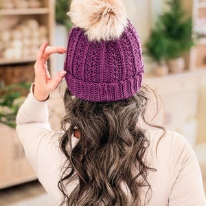 Purple crochet beanie with folded brim and faux fur pom pom shown from behind on long wavy hair