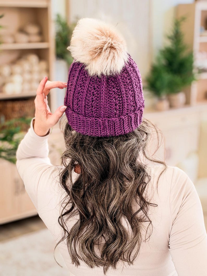 Purple crochet beanie with folded brim and faux fur pom pom shown from behind on long wavy hair