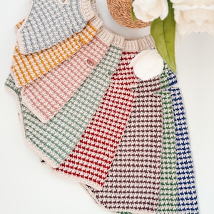 May include: A collection of sleeveless crochet vests arranged in a fan shape. Each vest features a two-tone striped pattern with a cream-colored base and alternating colors including blue, yellow, pink, green, red, brown, and dark blue.