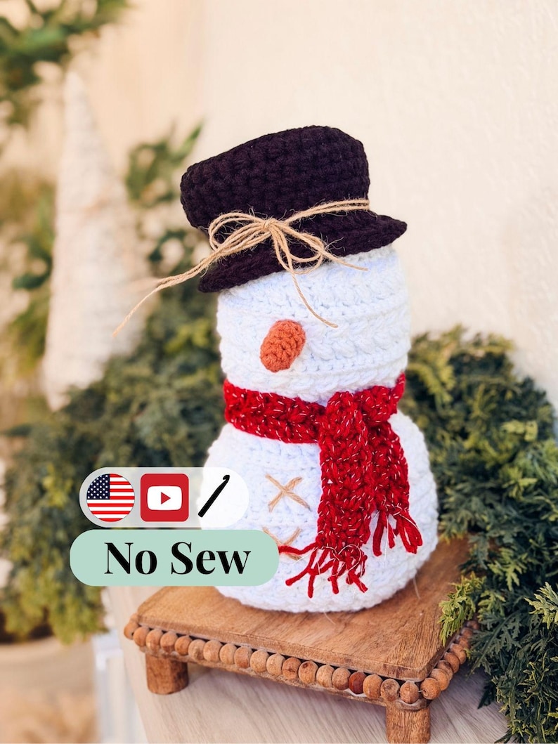 White crochet snowman with brown twine-tied hat, red scarf and twine X buttons on a beaded wooden riser