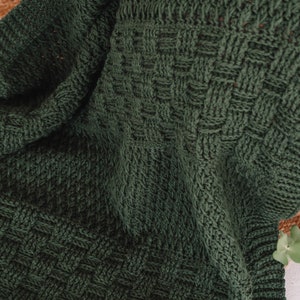 Puede incluir: Una manta tejida de color verde bosque oscuro que presenta un patr&oacute;n de textura de tejido de cesta. La tela muestra una construcci&oacute;n de puntadas densa y uniforme con un borde acanalado, exhibiendo un color profundo y s&oacute;lido en toda la pieza.