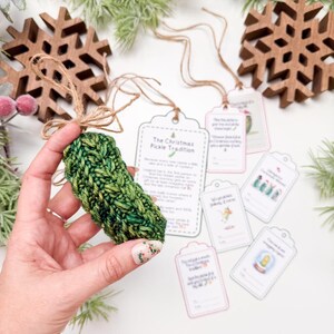 May include: A crocheted green pickle ornament with a jute twine loop, accompanied by several rectangular paper gift tags featuring printed text and illustrations related to the Christmas pickle tradition, including a larger instruction card.